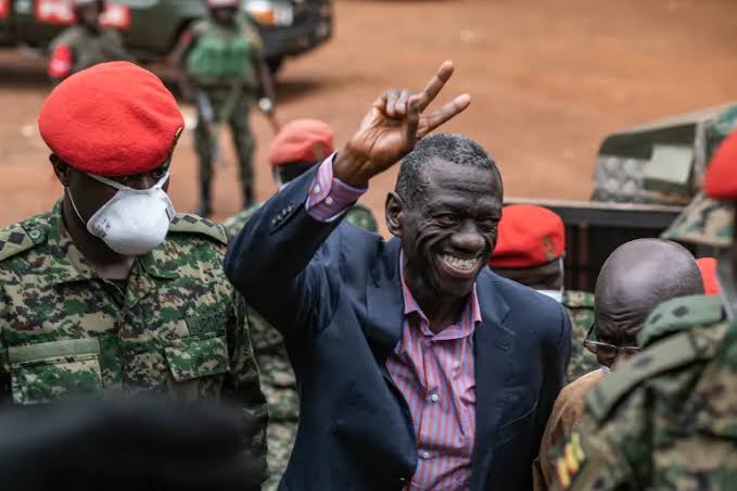 Dr. Kizza Besigye flashing a victory sign while flanked by Ugandan military personnel